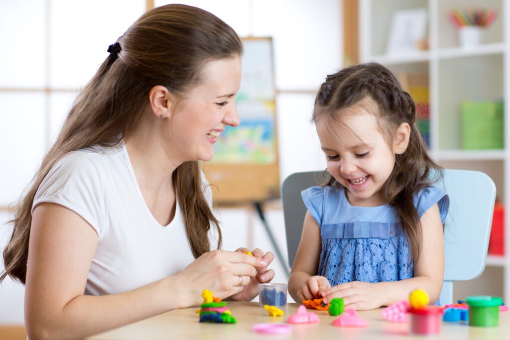A Girl child and teacher playing clay and laughing
